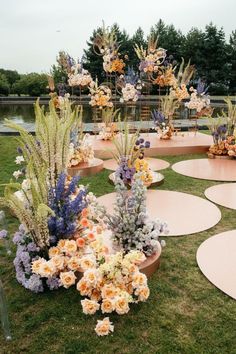 an arrangement of flowers and plants on display in the grass near a body of water