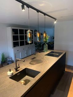 a kitchen counter with two sinks and three hanging lights