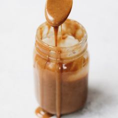 caramel sauce being drizzled over ice cream in a glass jar with a spoon