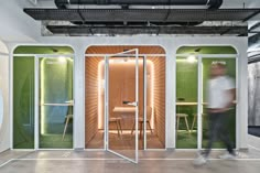 a man walking into a room with green walls and glass doors on both sides, while another person walks in the doorway