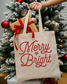 a person holding a bag in front of a christmas tree that says, jolly merry happy joy