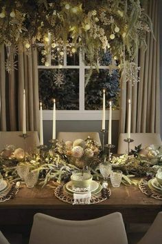 a dining room table set for christmas with candles and greenery on the table top