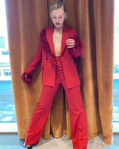 a woman in a red suit leaning against a curtain with her hands on her hips