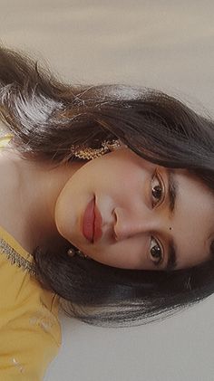 a young woman with long hair wearing a yellow shirt and gold jewelry is posing for the camera