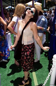 a woman standing in front of a group of people at an outdoor event wearing sun glasses