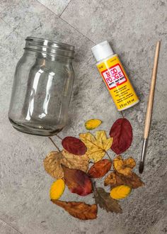 autumn leaves and glue sitting on top of a cement floor next to a glass jar