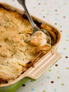 a green casserole dish with shrimp and potatoes in it on a polka dot tablecloth