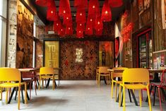 an empty restaurant with yellow chairs and red lights hanging from the ceiling, along with other tables and chairs