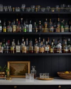 an assortment of liquor bottles and glasses on a shelf in a room with black walls