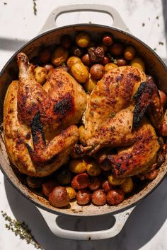 a pan filled with chicken, potatoes and olives on top of a white table