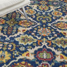 a blue and yellow area rug with an ornate design on the bottom, in front of a white bench