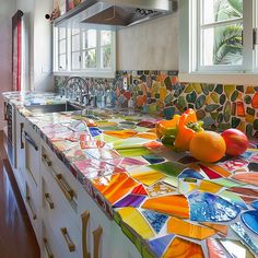 a kitchen counter with colorful tiles on it and fruit sitting on the counter top in front of an open window