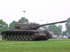 an old tank sitting on top of a lush green field next to a parking lot