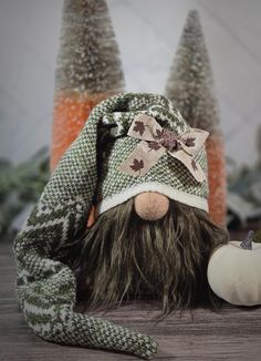 a stuffed animal wearing a knitted hat next to some small trees and pumpkins