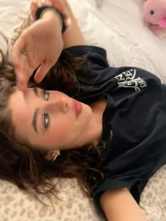 a woman laying on top of a bed next to a pink teddy bear and wearing a black shirt