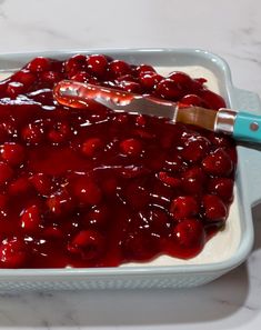 a white dish filled with cherries sitting on top of a marble counter next to a blue spatula