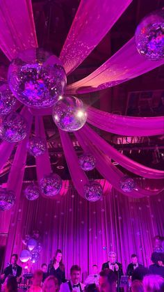 people are sitting at tables in front of purple lights and disco balls hanging from the ceiling