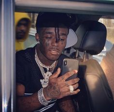 a man sitting in the back seat of a car looking at his cell phone while wearing a hat