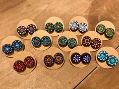 twelve pairs of wooden earring studs with multicolored dots on them sitting on a table