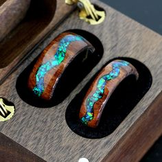 two wooden rings with green and blue opal inlays on them sitting inside a box