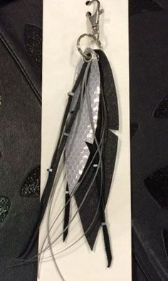 a feather keychain is hanging from a white card with black and silver feathers