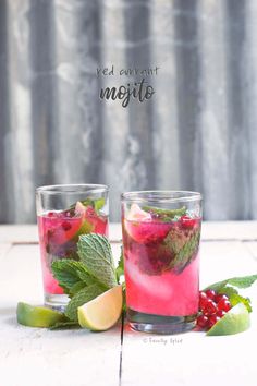 two glasses filled with fruit and mint mojito next to each other on a table