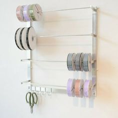 a white wall mounted shelf filled with different types of spools of thread and scissors