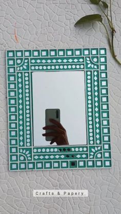 a hand holding a cell phone in front of a green and white square shaped mirror