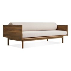 a wooden couch with white pillows on it's back and arm rests against the wall