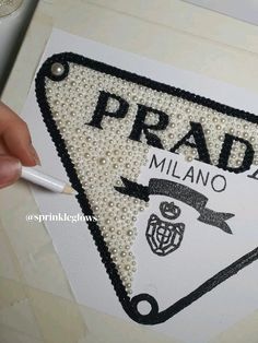 a hand is holding a piece of paper with beading on it that says prada millano