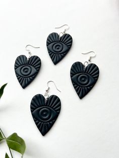 three black heart shaped earrings sitting on top of a white table next to a plant