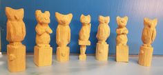 seven wooden carved cats lined up in a row on a table next to a blue wall