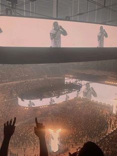 a large crowd at a concert with their hands up in the air and two men on stage