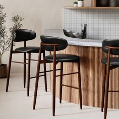 three bar stools sitting in front of a counter with a potted plant next to it