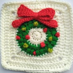 a crocheted square with a red bow on it and a green wreath in the center