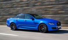 a blue car driving down the road with rocks in the backgroud behind it