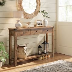 a wooden table sitting in front of a window next to a rug and potted plant