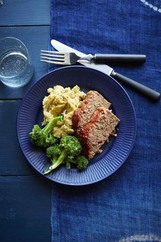 a blue plate topped with meat and veggies next to a glass of water