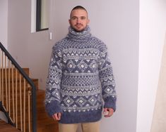 a man standing in front of a stair case wearing a blue sweater and tan pants