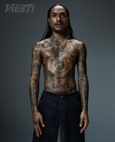 a man with tattoos standing in front of a gray background