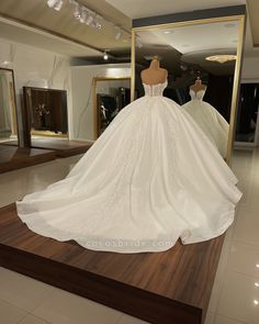 a wedding dress on display in front of a mirror and mannequins behind it