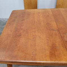 a wooden table with two chairs next to it on concrete floored area in front of white wall