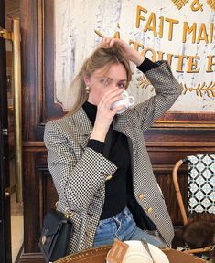 a woman sitting at a table drinking from a cup