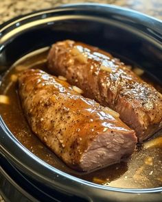 two pieces of meat in a slow cooker with some sauce on the side,