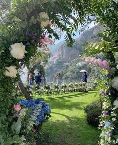 people are standing under an archway with flowers on the lawn and in the background is mountains