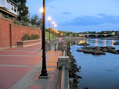 a lamp post on the side of a river next to a sidewalk and bridge at night