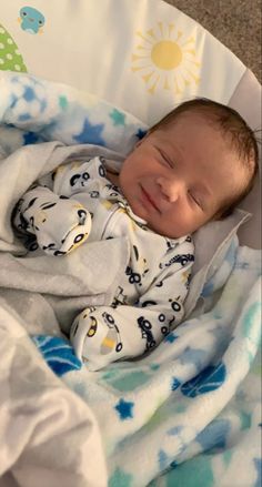 a baby is laying in a bed with a blanket on it's back and smiling