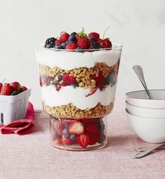 a bowl of granola with berries and yogurt in it next to two bowls of strawberries