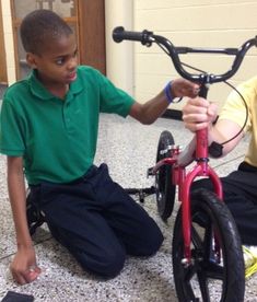 two boys sitting on the floor next to their bikes and one boy is touching the handlebars