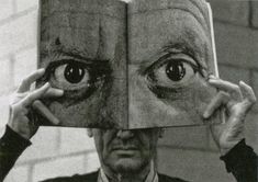 a man holding up an open book to his face with two large eyes on it